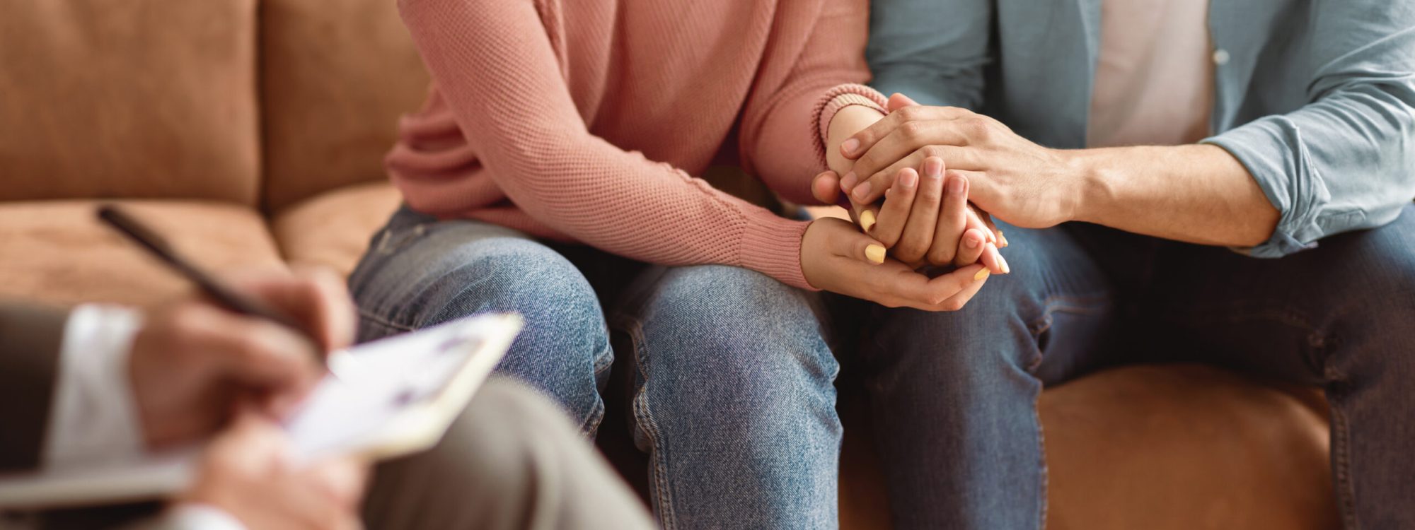Ehepaar in einer Sitzung mit einem Eheberater, Hand in Hand haltend, während der Therapeut Notizen macht